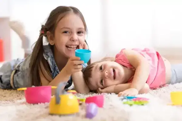 Two young kids laughing and playing on the floor