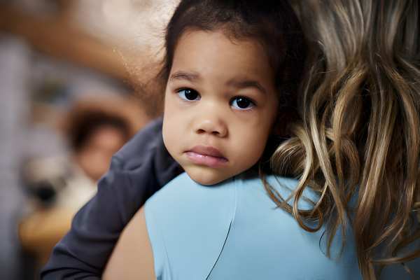 Toddler girl being held and hugged on the shoulder of her adopted mother 