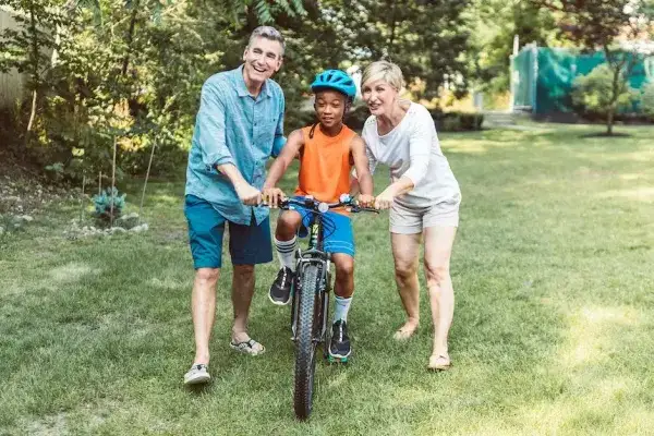 Two foster parents supporting a school-age child on a bike in the grass