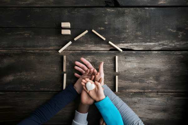 Four family member hands stacked on top of each other over a rustic picture of a home