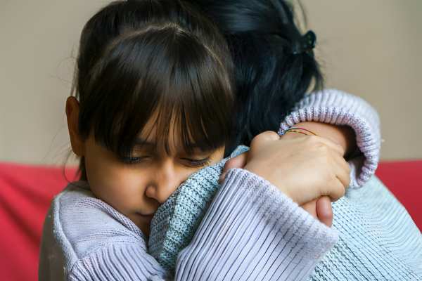 Foster-to-Adopt mom hugs and consoles a young girl, hugging with head on Mom's shoulder