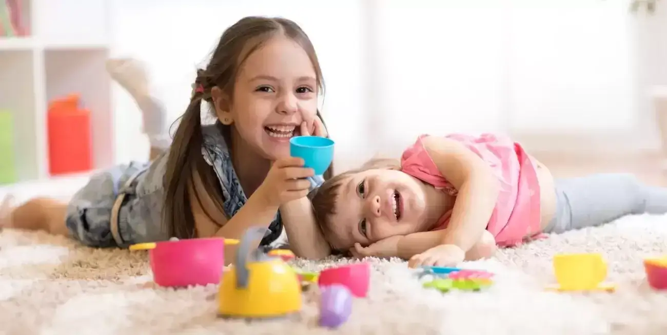 Two young kids laughing and playing on the floor